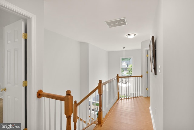 hall with baseboards, light wood-style floors, an upstairs landing, and visible vents
