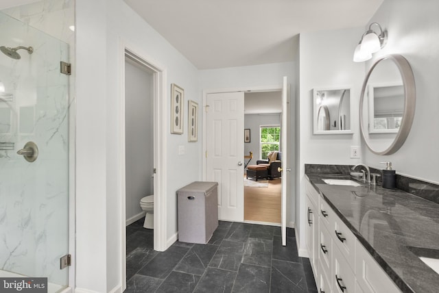bathroom featuring baseboards, toilet, a sink, double vanity, and a marble finish shower