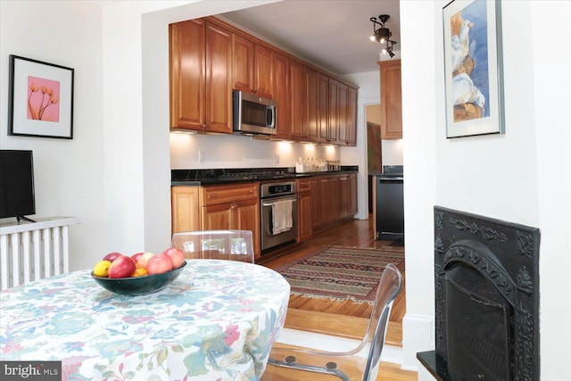 kitchen featuring dark countertops, appliances with stainless steel finishes, a fireplace, brown cabinetry, and wood finished floors