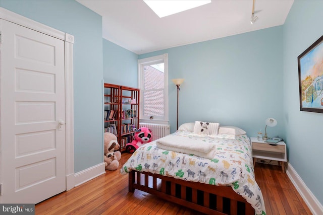 bedroom with radiator, baseboards, rail lighting, and hardwood / wood-style floors