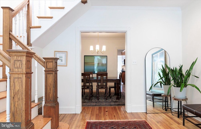 foyer entrance with crown molding, an inviting chandelier, stairs, baseboards, and light wood-type flooring