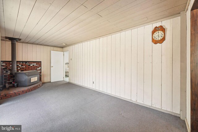unfurnished living room featuring wooden ceiling, carpet, a wood stove, and wood walls