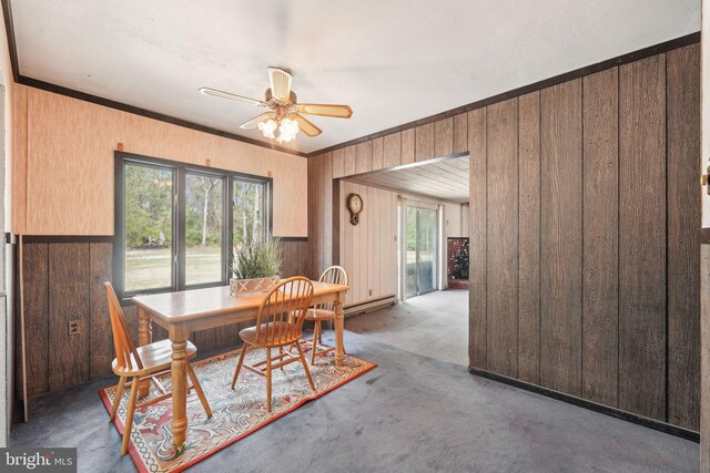 carpeted dining space with crown molding, wood walls, a ceiling fan, and a baseboard radiator