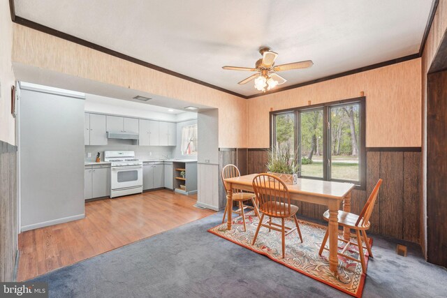 dining area with visible vents, wood walls, a ceiling fan, and ornamental molding