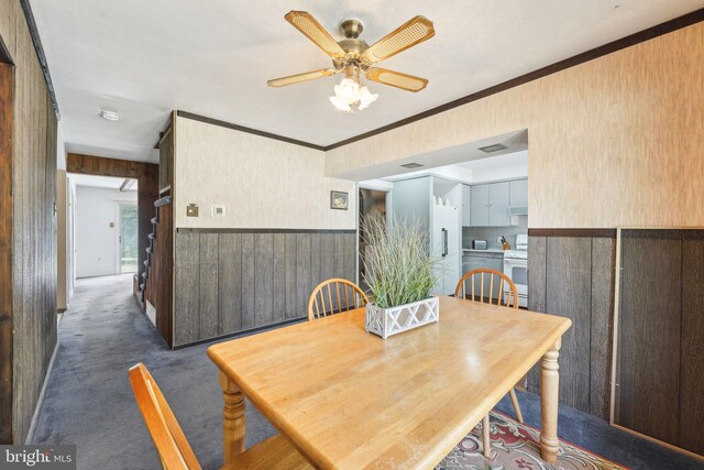 dining room with ceiling fan, crown molding, a wainscoted wall, carpet floors, and wooden walls