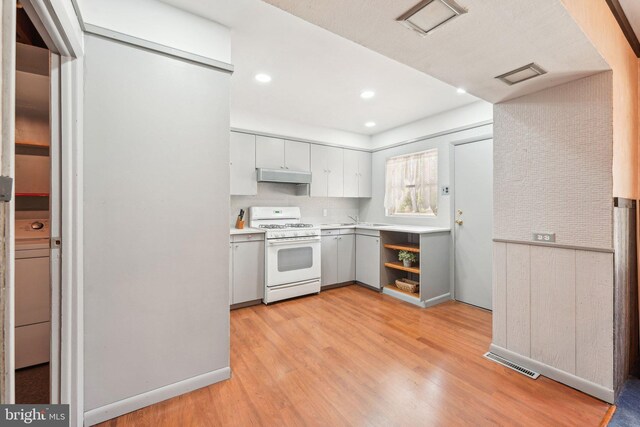 kitchen featuring light wood finished floors, light countertops, under cabinet range hood, visible vents, and white range with gas cooktop