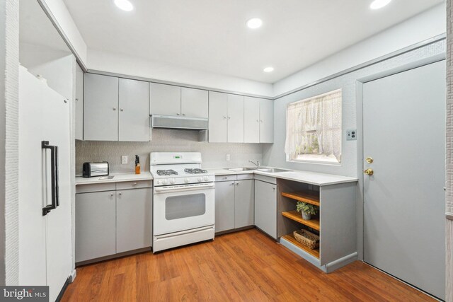 kitchen with gray cabinets, gas range gas stove, a sink, under cabinet range hood, and high end fridge