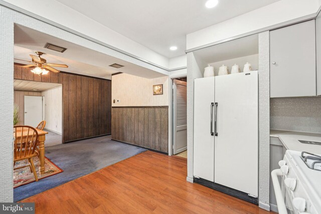 kitchen with visible vents, white appliances, light wood-style floors, ceiling fan, and wooden walls