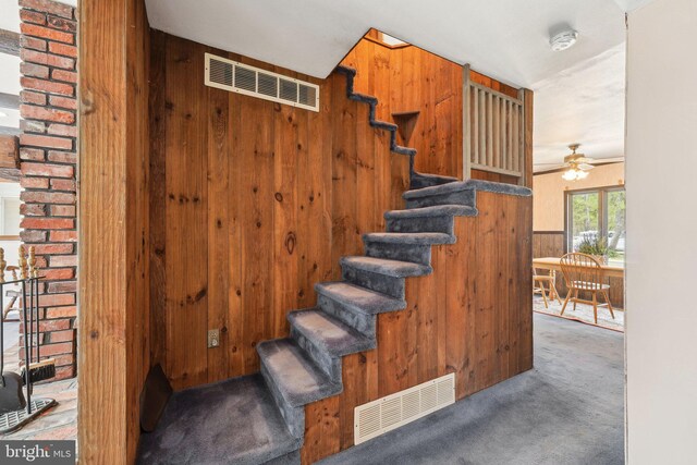 staircase with visible vents, wood walls, carpet, and ceiling fan