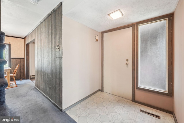corridor with a textured ceiling, visible vents, baseboards, a baseboard heating unit, and light floors