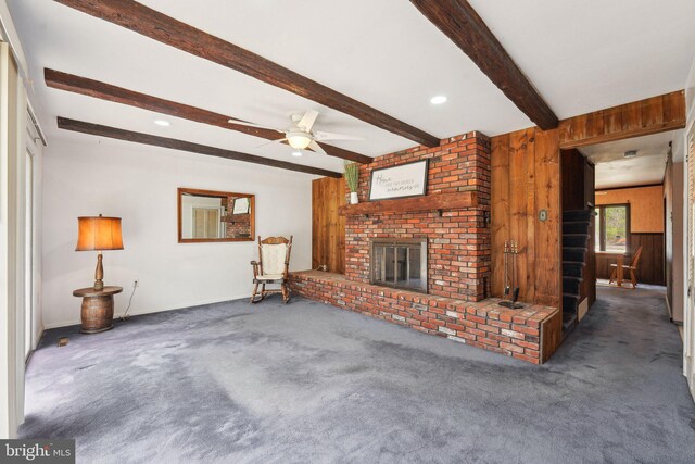 unfurnished living room featuring a fireplace, carpet flooring, wood walls, and beam ceiling