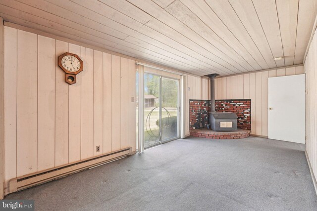 unfurnished living room with a wood stove, wooden ceiling, a baseboard heating unit, wooden walls, and carpet flooring