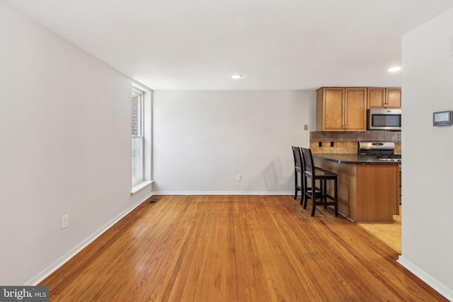 18 University Mews, Philadelphia, PA 19104 - kitchen featuring gas range, dark countertops, stainless steel microwave, a breakfast bar, and light wood-style flooring