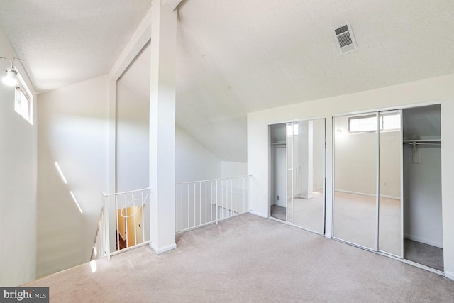 interior space featuring lofted ceiling, a textured ceiling, carpet floors, and visible vents