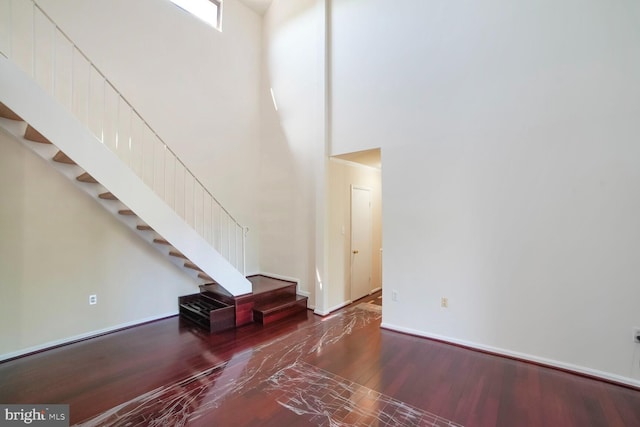 unfurnished living room with stairway, a high ceiling, baseboards, and wood finished floors