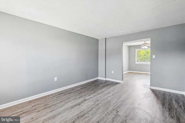 empty room with a textured ceiling, baseboards, ceiling fan, and wood finished floors