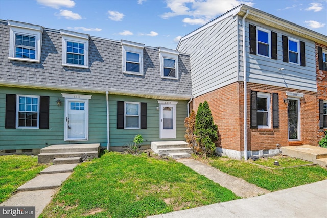 townhome / multi-family property with brick siding, mansard roof, roof with shingles, and a front lawn