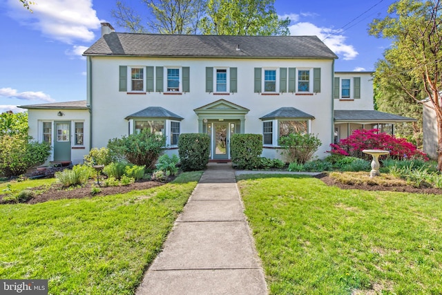 colonial inspired home with a front lawn, stucco siding, and a chimney