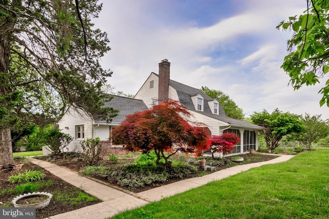 view of home's exterior featuring a yard, a chimney, a sunroom, roof with shingles, and brick siding
