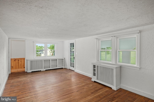 spare room with a textured ceiling, a textured wall, wood finished floors, radiator heating unit, and baseboards