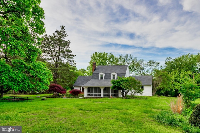 cape cod house featuring a sunroom, a front lawn, a chimney, and a shingled roof