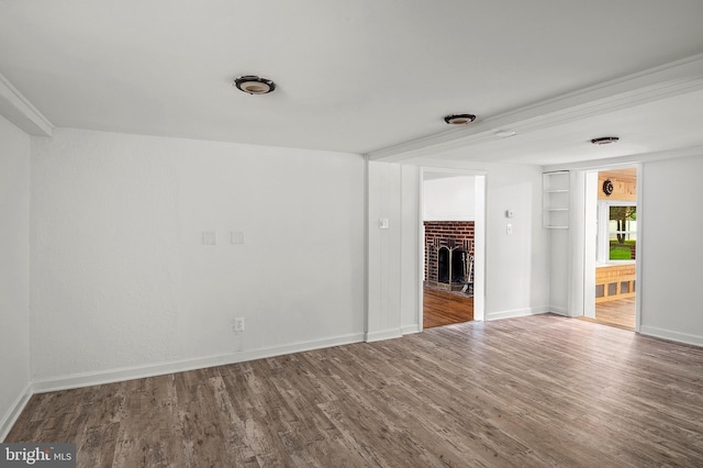 spare room featuring wood finished floors, a brick fireplace, and baseboards
