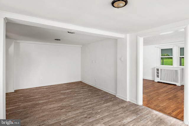 unfurnished room featuring wood finished floors, radiator heating unit, and baseboards