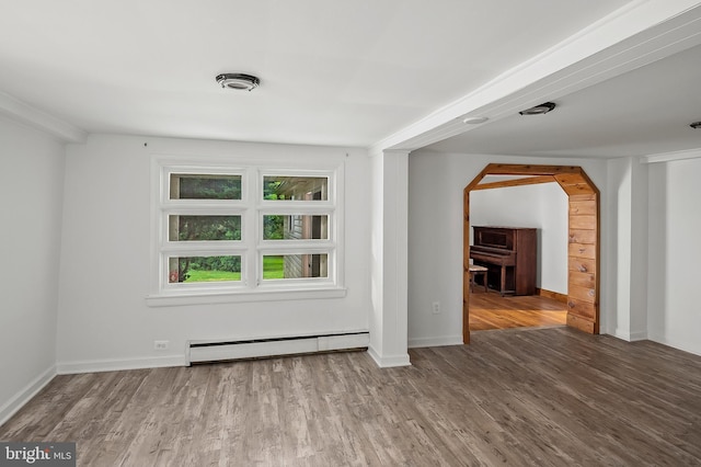 unfurnished room featuring baseboard heating, wood finished floors, arched walkways, and baseboards