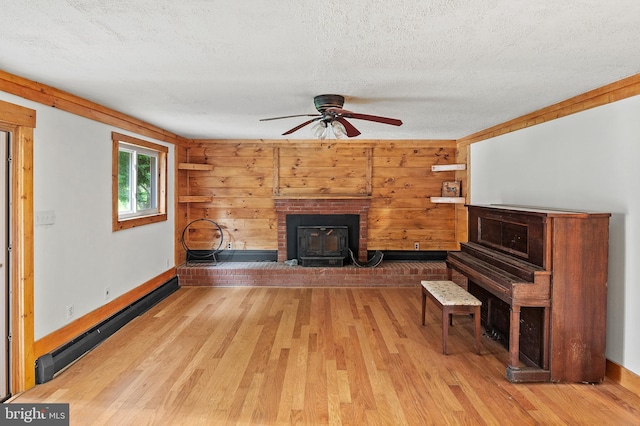 unfurnished living room featuring baseboard heating, light wood finished floors, a wood stove, baseboards, and a textured ceiling