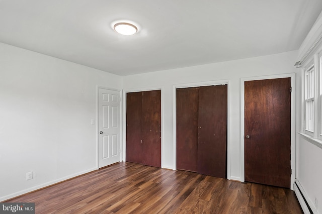 unfurnished bedroom with baseboard heating, two closets, wood finished floors, and baseboards