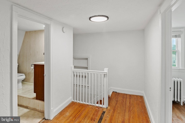 hall featuring an upstairs landing, radiator heating unit, wood finished floors, and baseboards