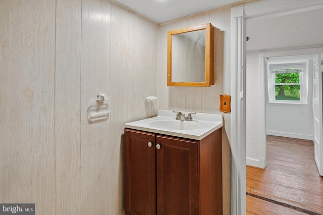 bathroom featuring vanity, wood finished floors, baseboards, and wood walls