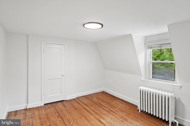 bonus room with radiator, light wood-type flooring, and baseboards