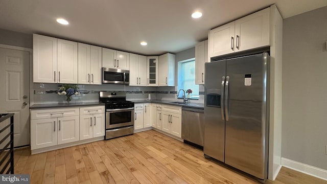 kitchen featuring dark countertops, stainless steel appliances, light wood finished floors, and white cabinetry