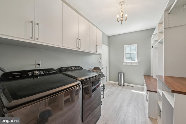 washroom featuring light wood-style floors, baseboards, washer and clothes dryer, cabinet space, and a notable chandelier