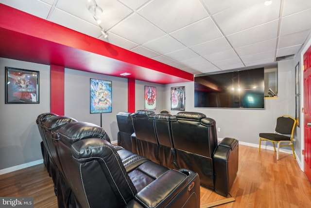 home theater room featuring baseboards, a drop ceiling, and wood finished floors
