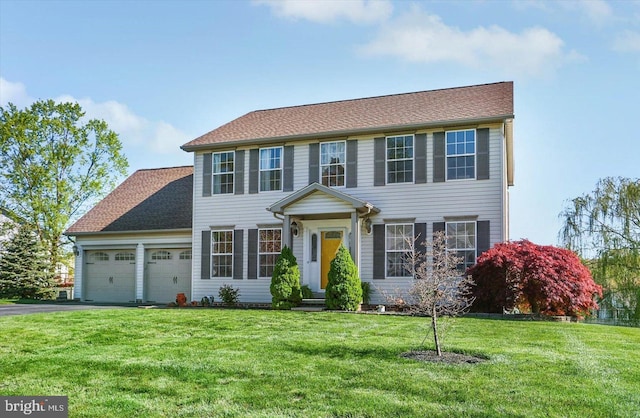 colonial-style house featuring an attached garage, driveway, and a front yard