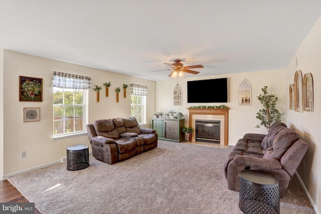 living area featuring a fireplace with flush hearth, baseboards, ceiling fan, and carpet flooring