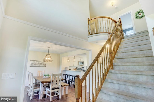 stairs with an inviting chandelier, ornamental molding, baseboards, and a towering ceiling