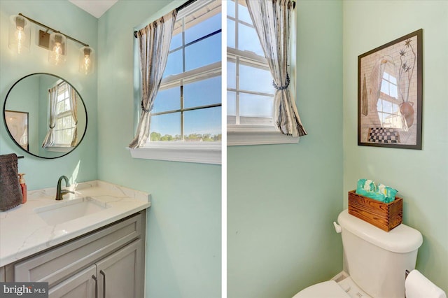 half bathroom with toilet, a healthy amount of sunlight, and vanity