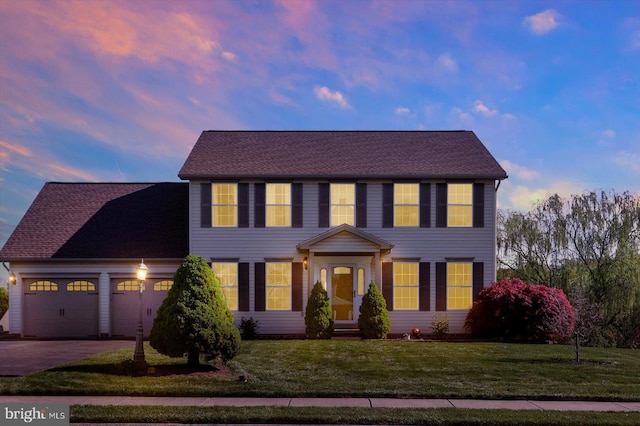 colonial home with a lawn, an attached garage, and aphalt driveway