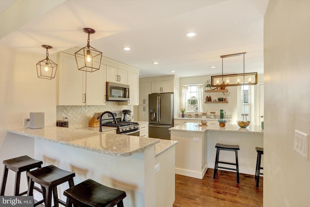 kitchen with light stone counters, a peninsula, backsplash, and stainless steel appliances