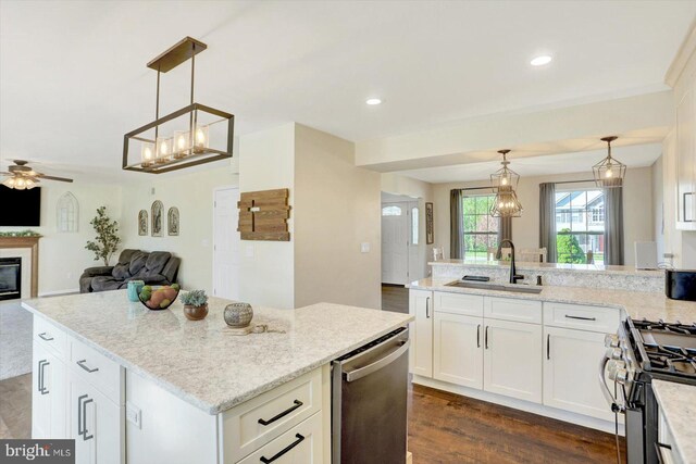 kitchen with appliances with stainless steel finishes, light stone countertops, a sink, white cabinets, and open floor plan