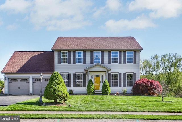 colonial home featuring roof with shingles, driveway, a front yard, and a garage