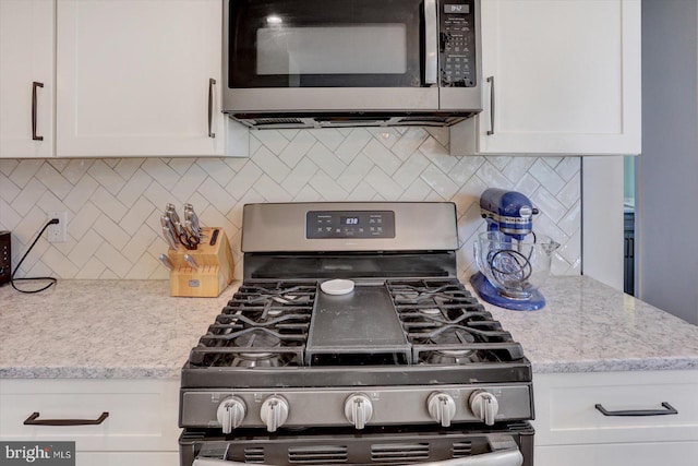 kitchen with appliances with stainless steel finishes, white cabinets, light stone countertops, and tasteful backsplash