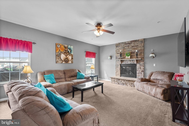 carpeted living room featuring baseboards, a stone fireplace, and ceiling fan
