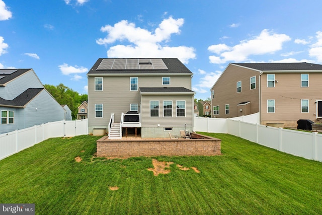 rear view of property featuring a fenced backyard, solar panels, and a yard