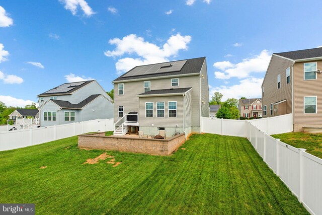 back of house featuring a residential view, a fenced backyard, roof mounted solar panels, stairway, and a lawn