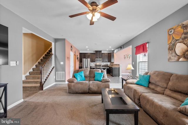 carpeted living room with stairway, baseboards, visible vents, and ceiling fan