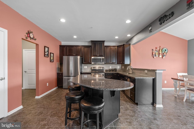 kitchen featuring dark brown cabinetry, stainless steel appliances, a kitchen bar, and a sink